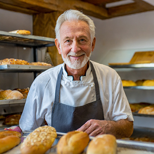 Bäckermeister vor einem Regal mit Backwaren lächelt in die Kamera